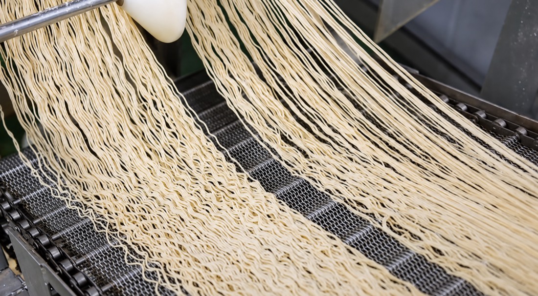 Wavy noodle strands moving along a mesh conveyor on the production line